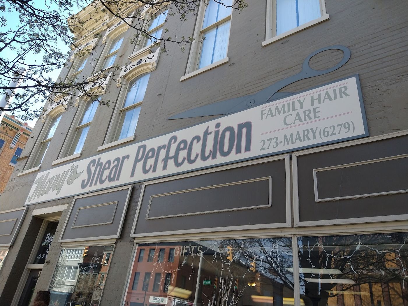 The Mary's Shear Perfection sign with a large pair of scissors above the storefront on a brick building on Main Street